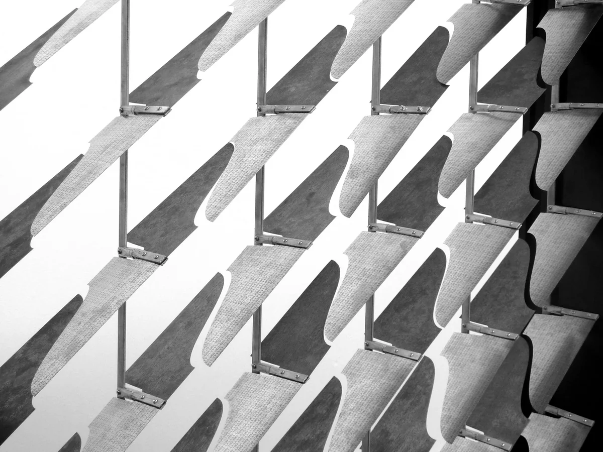 Diagonal bimetal fins rotate between glass panels to block sunlight without mechanical parts.