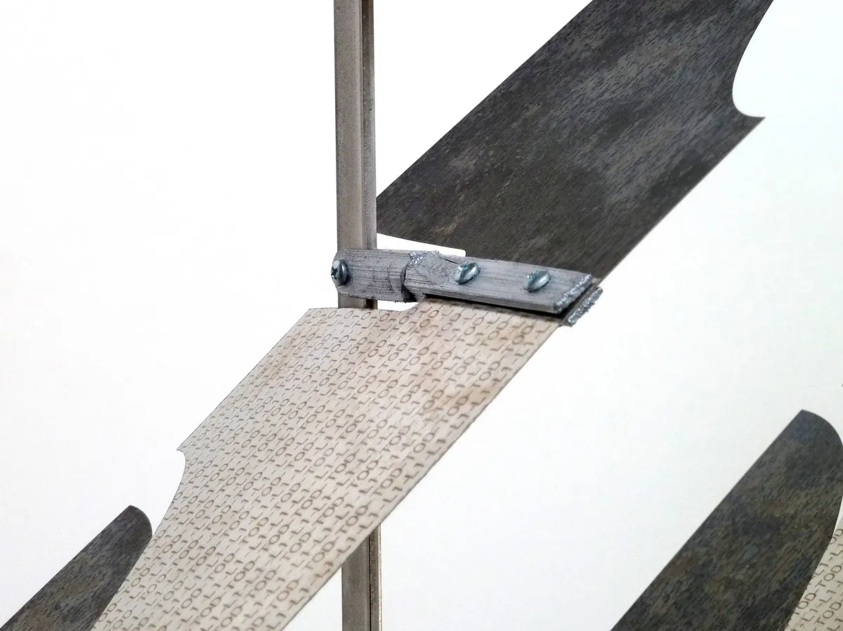 Close-up of bimetal fins rotating between glass panels, showing engraved binary code and thermal activation mechanism.
