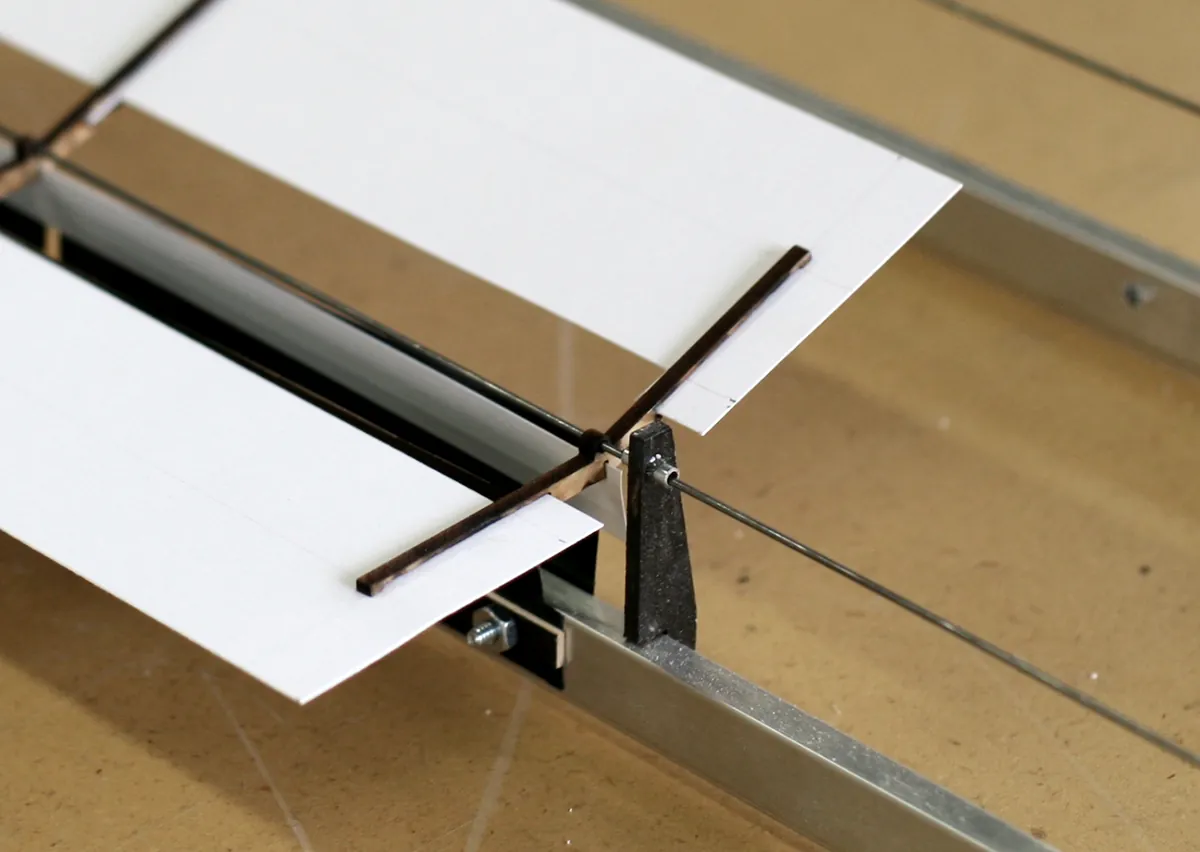 Close-up of a paper panel rotating on piano wire within a laser-cut wooden frame for solar tracking.